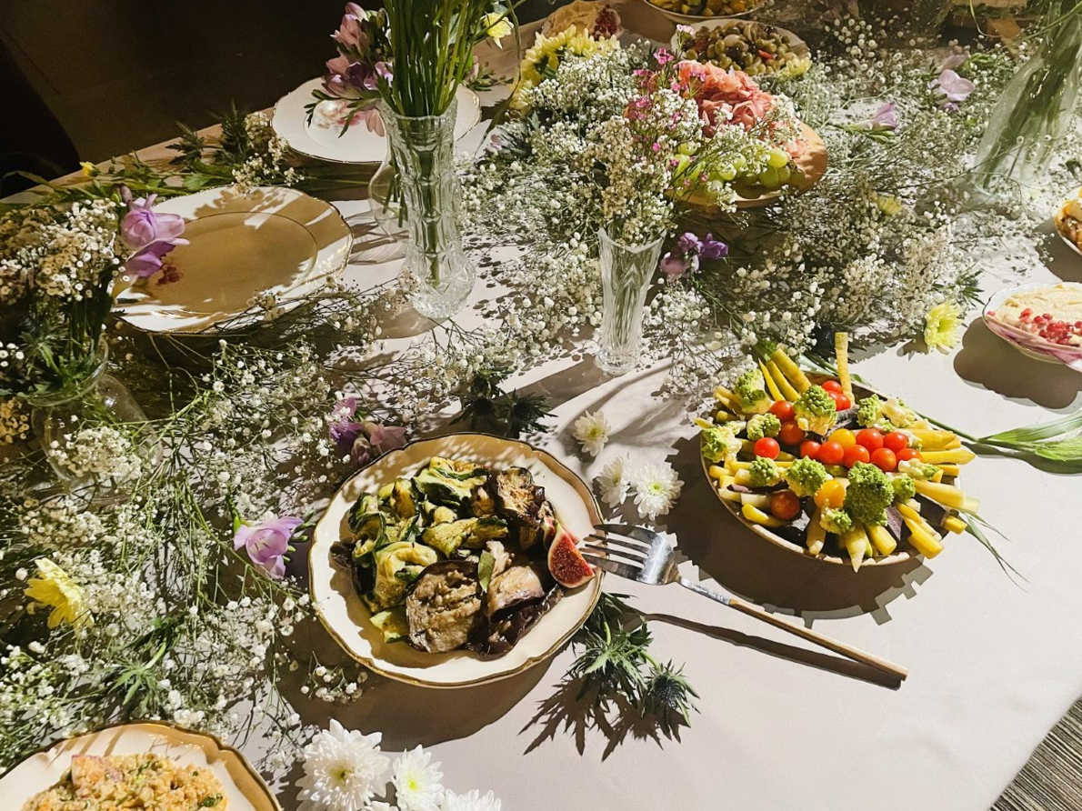 Une table dressée avec de la nourriture, décorée de fleurs, comprenant des assiettes de légumes et d'autres plats.