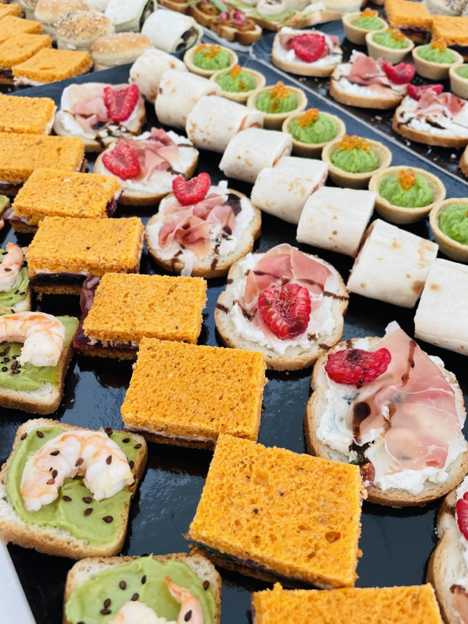 Assortiment d'entrées disposées sur un plateau noir : mini sandwichs, wraps et tartelettes avec diverses garnitures.