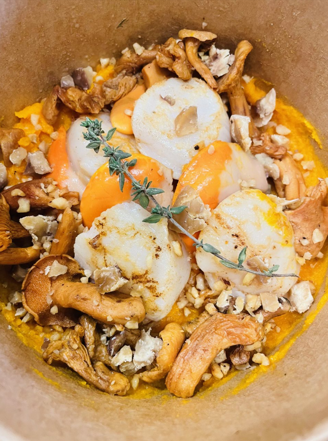 Pétoncles poêlés avec sauce dorée, champignons, noix et thym dans un bol en papier brun.