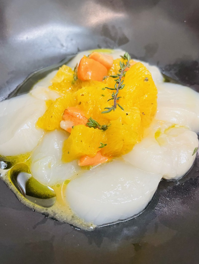 Plat de pétoncles aux segments d'orange, thym et huile d'olive, servi dans un bol noir.