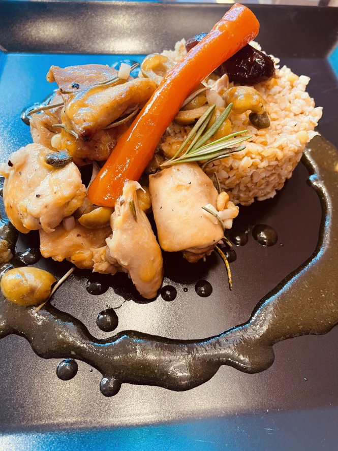 Plat de poulet et couscous aux légumes sur assiette noire.