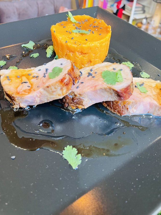 Filet de porc tranché avec patate douce et coriandre sur une assiette noire.