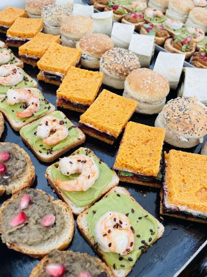 Entrées sur un plateau noir : crevettes sur toast à l'avocat, mini-burgers, sandwichs carrés et toasts avec garnitures.