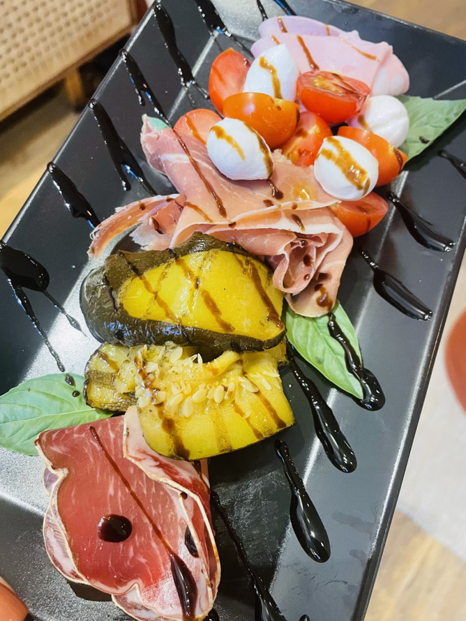 Une assiette de prosciutto, mozzarella, tomates et légumes grillés arrosés de glaçage balsamique.