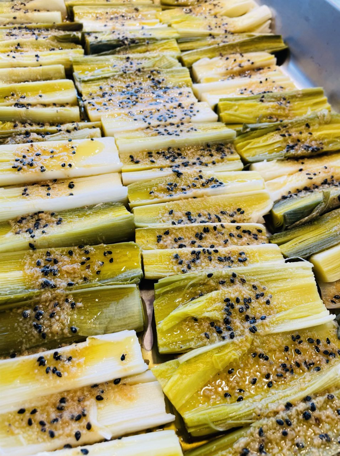 Poireaux émincés et glacés, parsemés de graines de sésame noir, disposés en rangées sur un plateau.