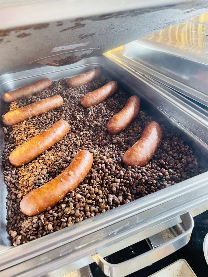 Saucisses dans un plateau chauffant sur des aliments foncés et granuleux.