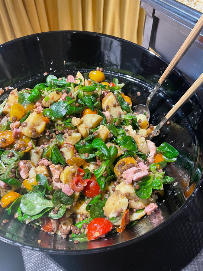 Salade dans un bol noir avec pommes de terre, lentilles, tomates cerises et légumes verts.