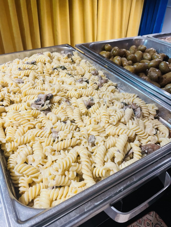 Plat de pâtes aux champignons dans un plateau buffet, accompagné d'un plateau de pommes de terre.
