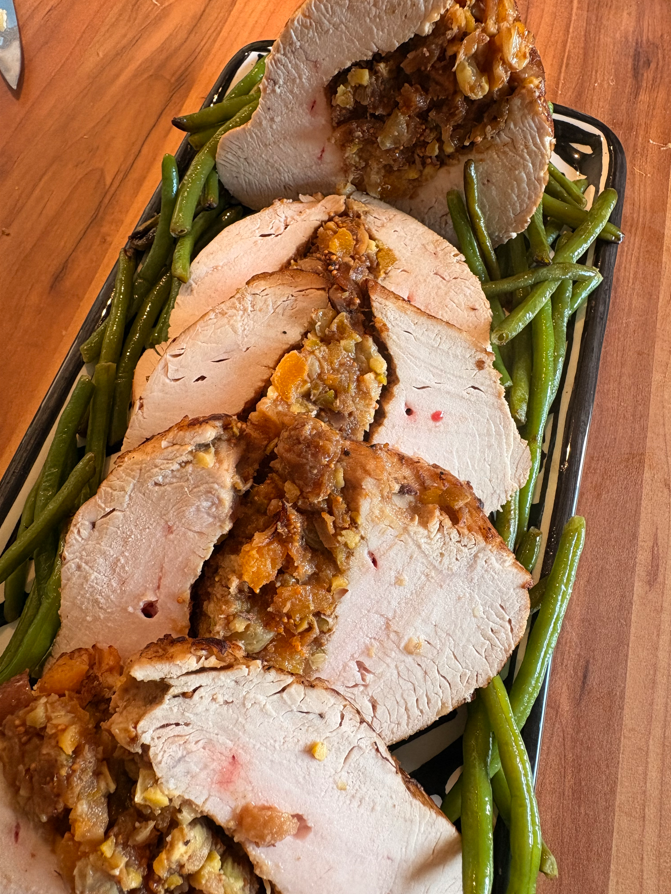 Poitrine de dinde farcie et tranchée sur un plateau avec des haricots verts.