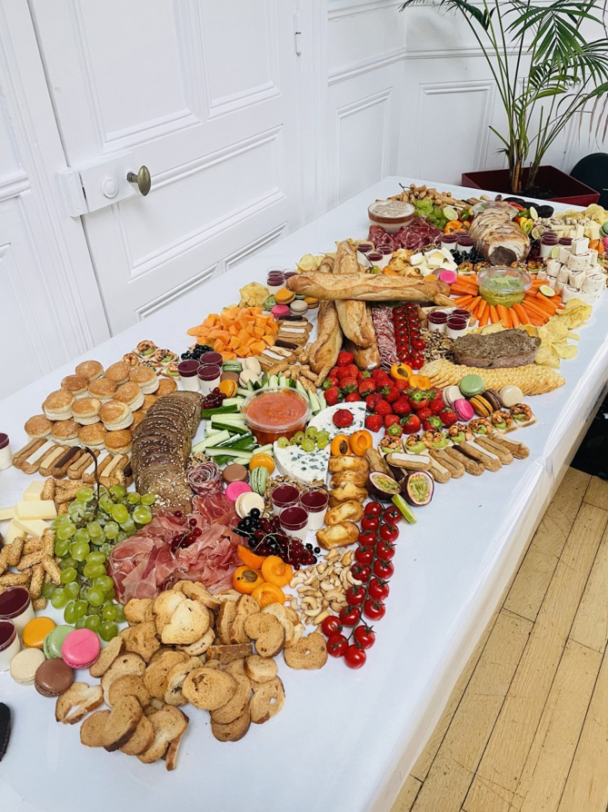 Grande planche de charcuterie sur une table blanche : fromages, viandes, fruits, craquelins et pain.