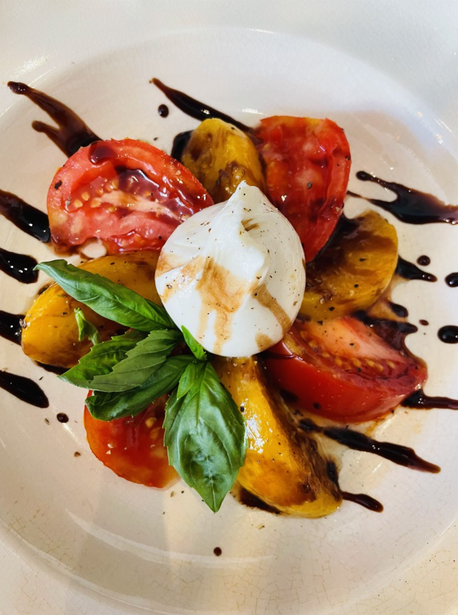 Salade Caprese avec tomates rouges et jaunes, mozzarella, basilic et glaçage balsamique sur une assiette blanche.
