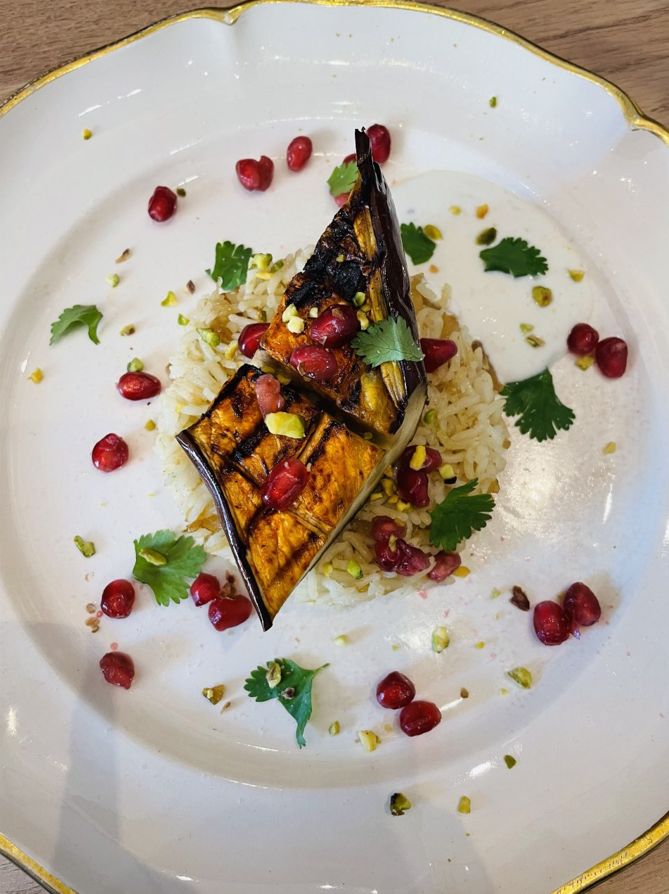 Aubergines grillées sur riz avec graines de grenade, pistaches et coriandre sur une assiette blanche.