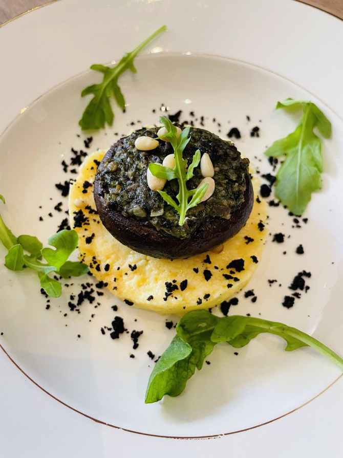 Champignons farcis au pesto et pignons de pin sur polenta, garnis de roquette et de poudre noire.