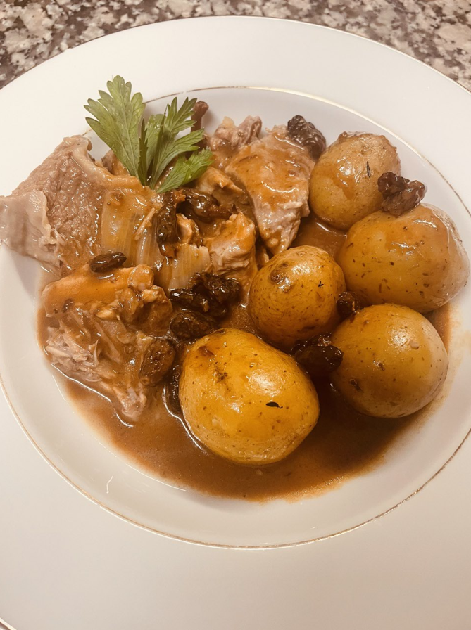 Ragoût d'agneau avec pommes de terre et raisins secs sur une assiette blanche, garni de persil.