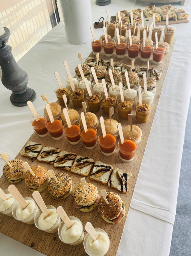 Planche en bois avec divers petits amuse-gueules : hamburgers, trempettes et craquelins avec garnitures.