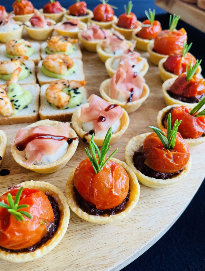Plateau d'amuse-gueules : fonds de tartelettes garnis de diverses garnitures, dont des tomates et des crevettes.