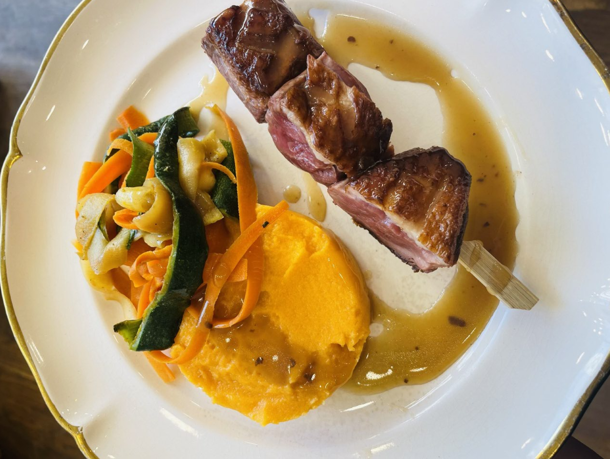 Brochettes de canard sur brochette, accompagnées de purée de patates douces et de légumes sautés, le tout servi avec sauce.