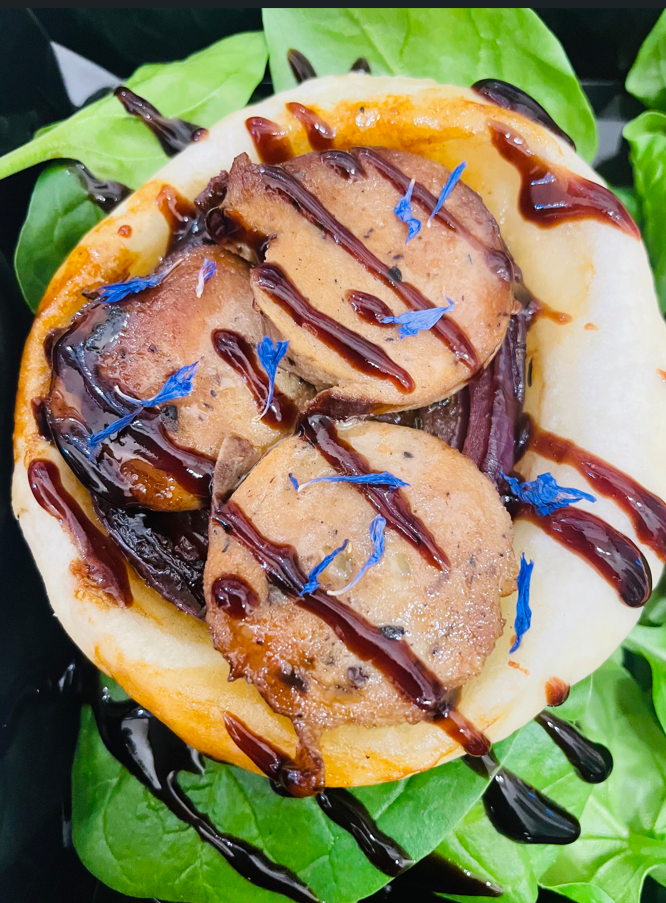 Trois médaillons poêlés sur un pain plié, arrosés de glaçage, parsemés de fleurs bleues, sur des épinards.