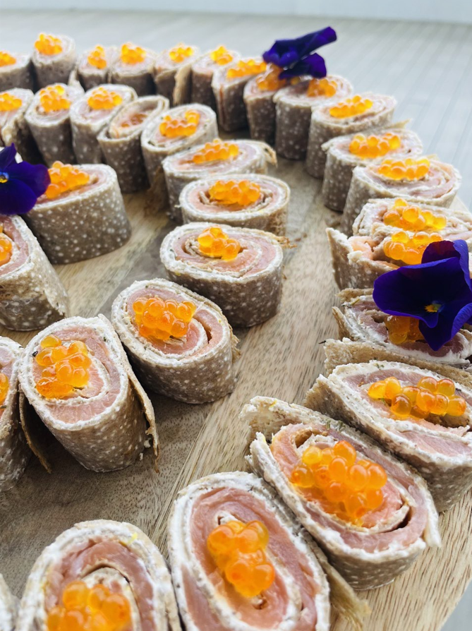 Apéritifs au saumon et au caviar disposés sur une planche en bois, garnis de fleurs.