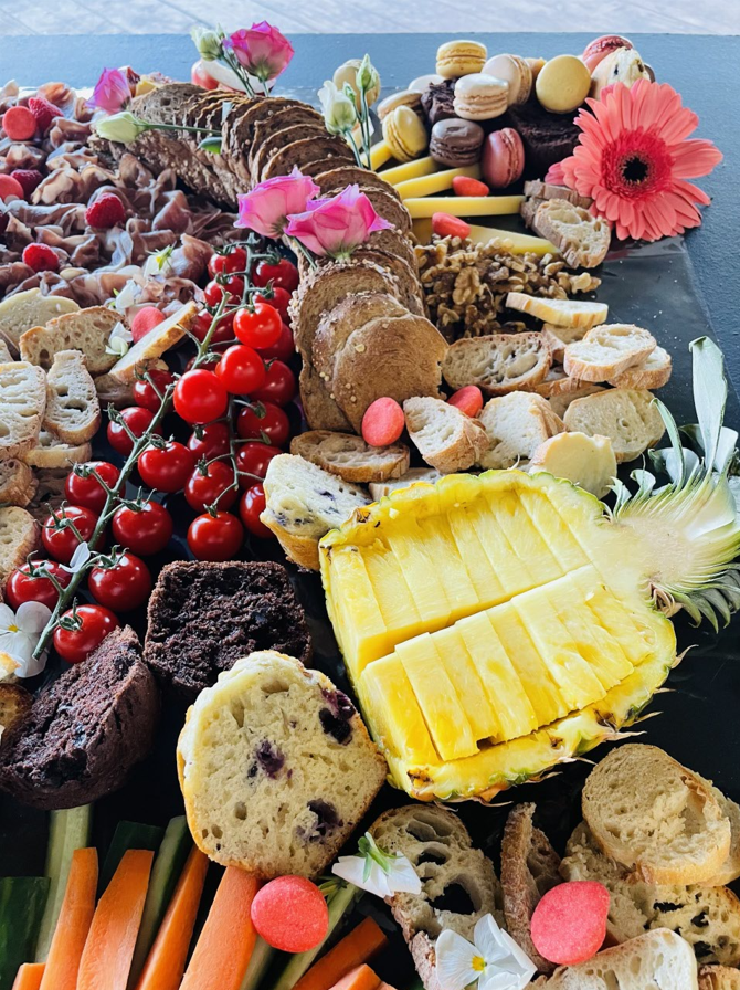 Planche de charcuterie avec divers aliments comme des craquelins, des fruits et des pâtisseries; décorée de fleurs.