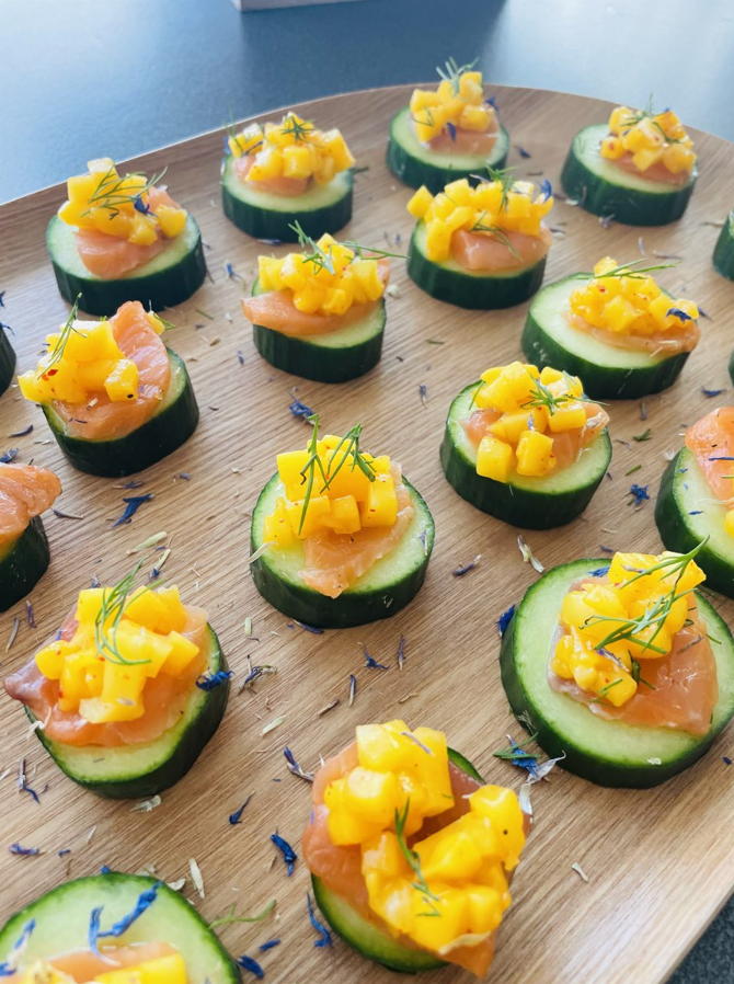 Bouchées de concombre au saumon et à la mangue sur un plateau en bois, garnies d'aneth.