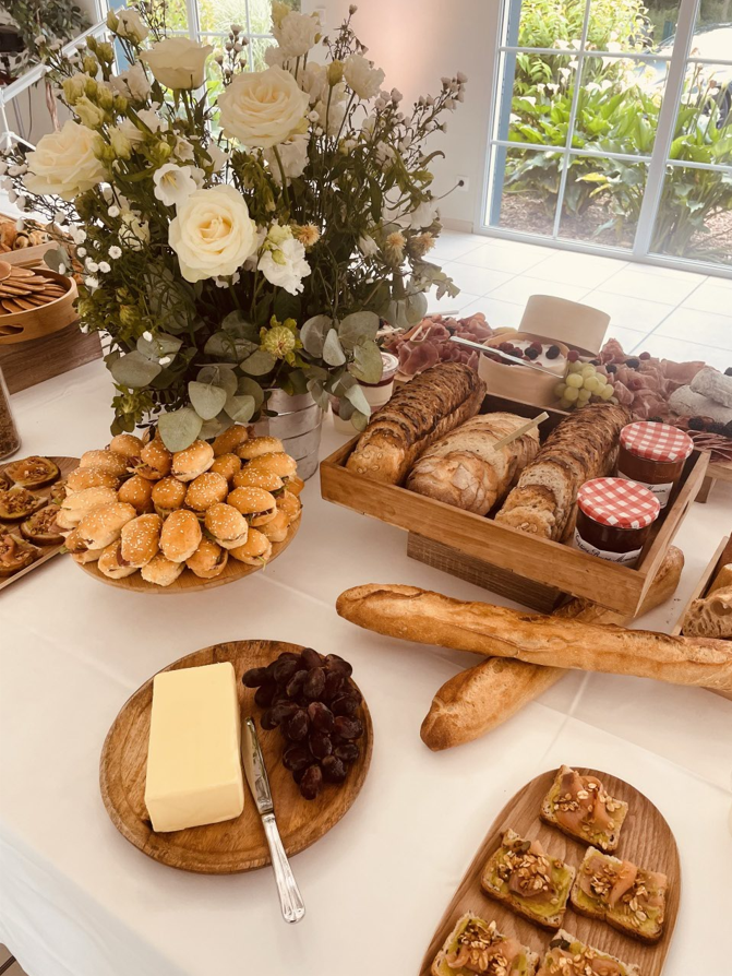 Planche de charcuterie avec pain, craquelins, fromage, raisins et fleurs sur une table recouverte de blanc.