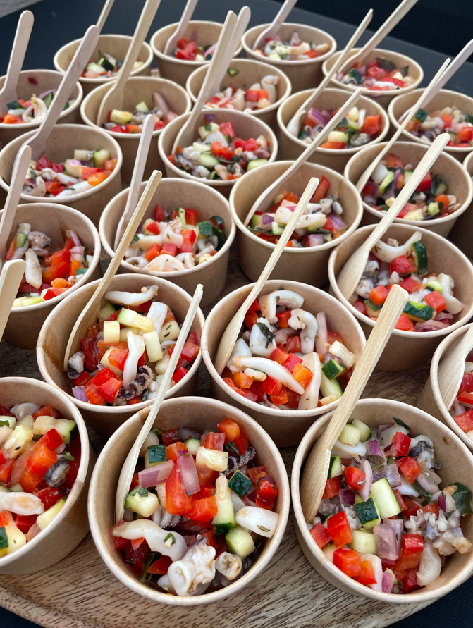 Petits gobelets en papier remplis de légumes et de fruits de mer hachés colorés, chacun avec une cuillère en bois.