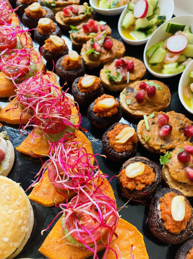 Assortiment d'entrées : mini-sandwichs, champignons farcis et petites tartelettes sur un plat de service noir.