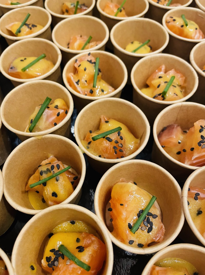 Petites portions de nourriture dans des gobelets en papier : saumon avec sauce et garniture.