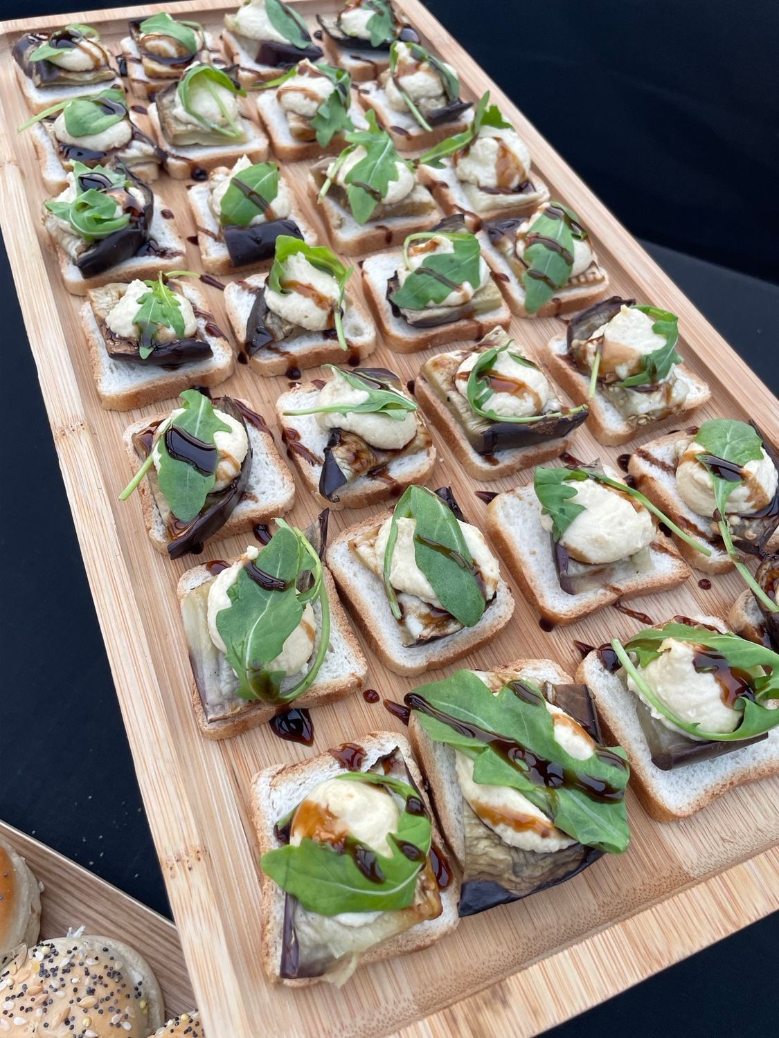 Entrées sur un plateau en bois : pain grillé, aubergine, mozzarella, roquette et glaçage balsamique.