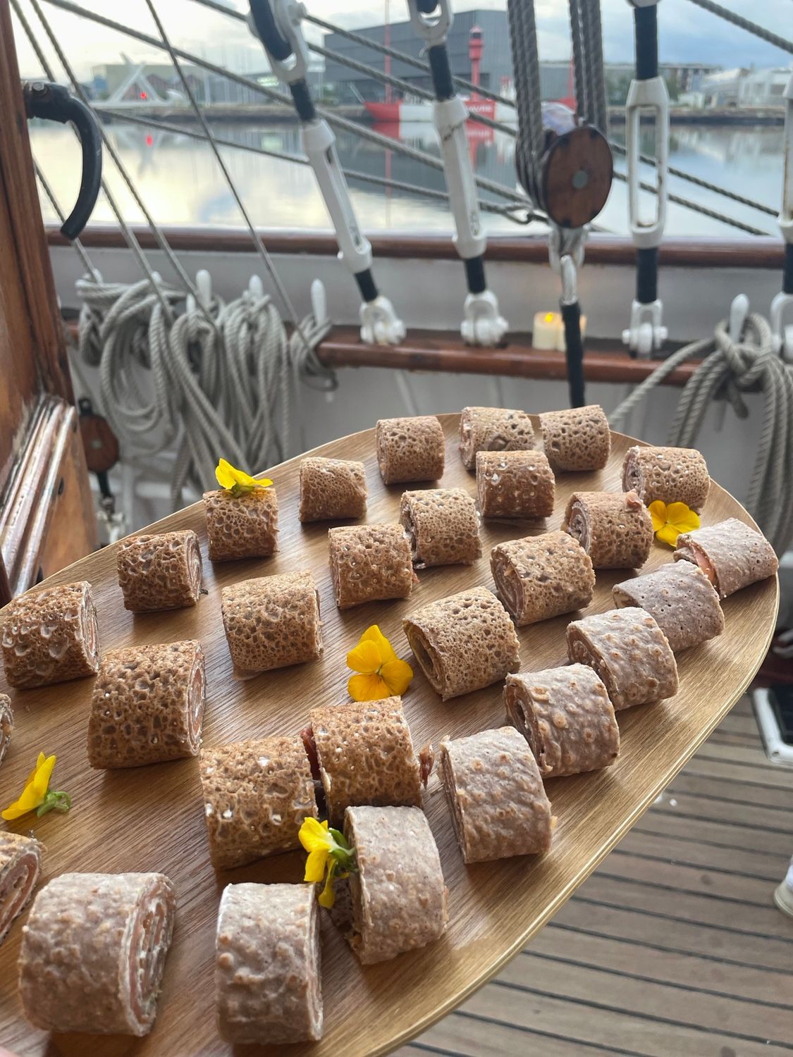 Plateau en bois avec des amuse-bouche roulés, garni de fleurs jaunes par Chez Bex, traiteur au Havre