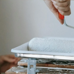 A man is standing on a ladder holding a paint roller.