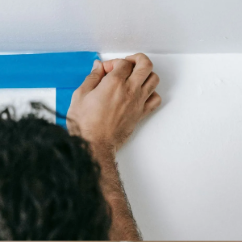 A man is painting a wall with blue tape.