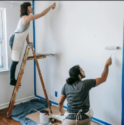A man and a woman are painting a wall in a room.