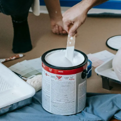 A person is mixing paint in a can with a brush.