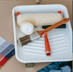 A paint tray with paint rollers , brushes and paint samples.