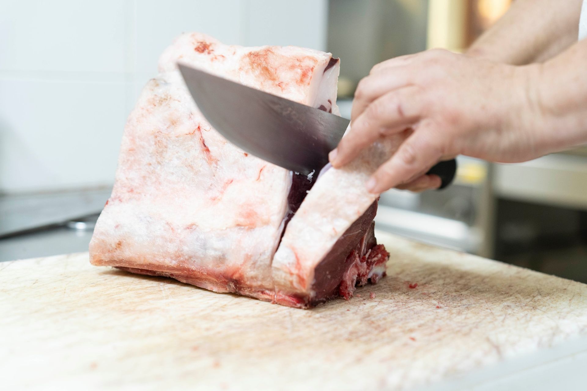 Macellaio che taglia la carne cruda con un grosso coltello su un tagliere bianco.