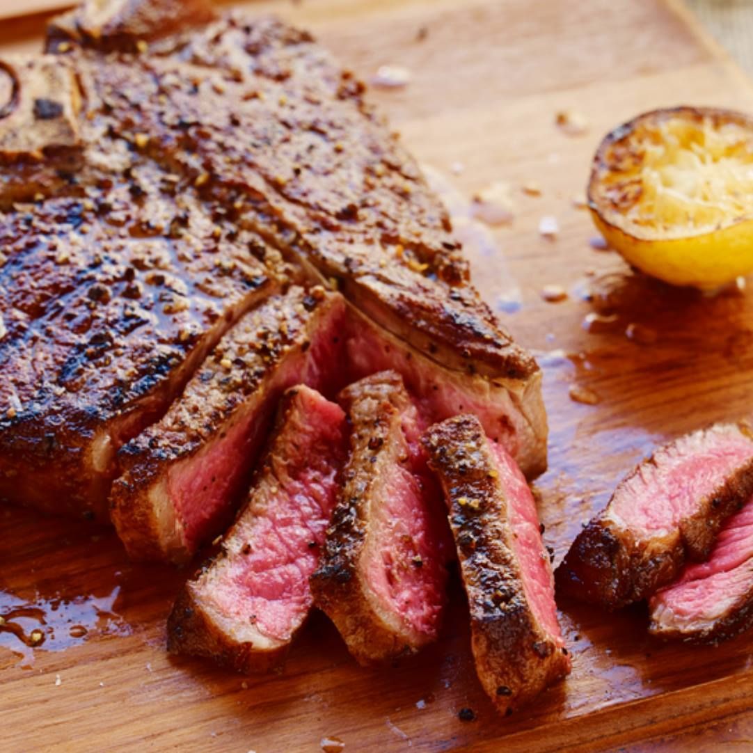 Bistecca tagliata a fette su un tagliere di legno, con mezzo limone grigliato.