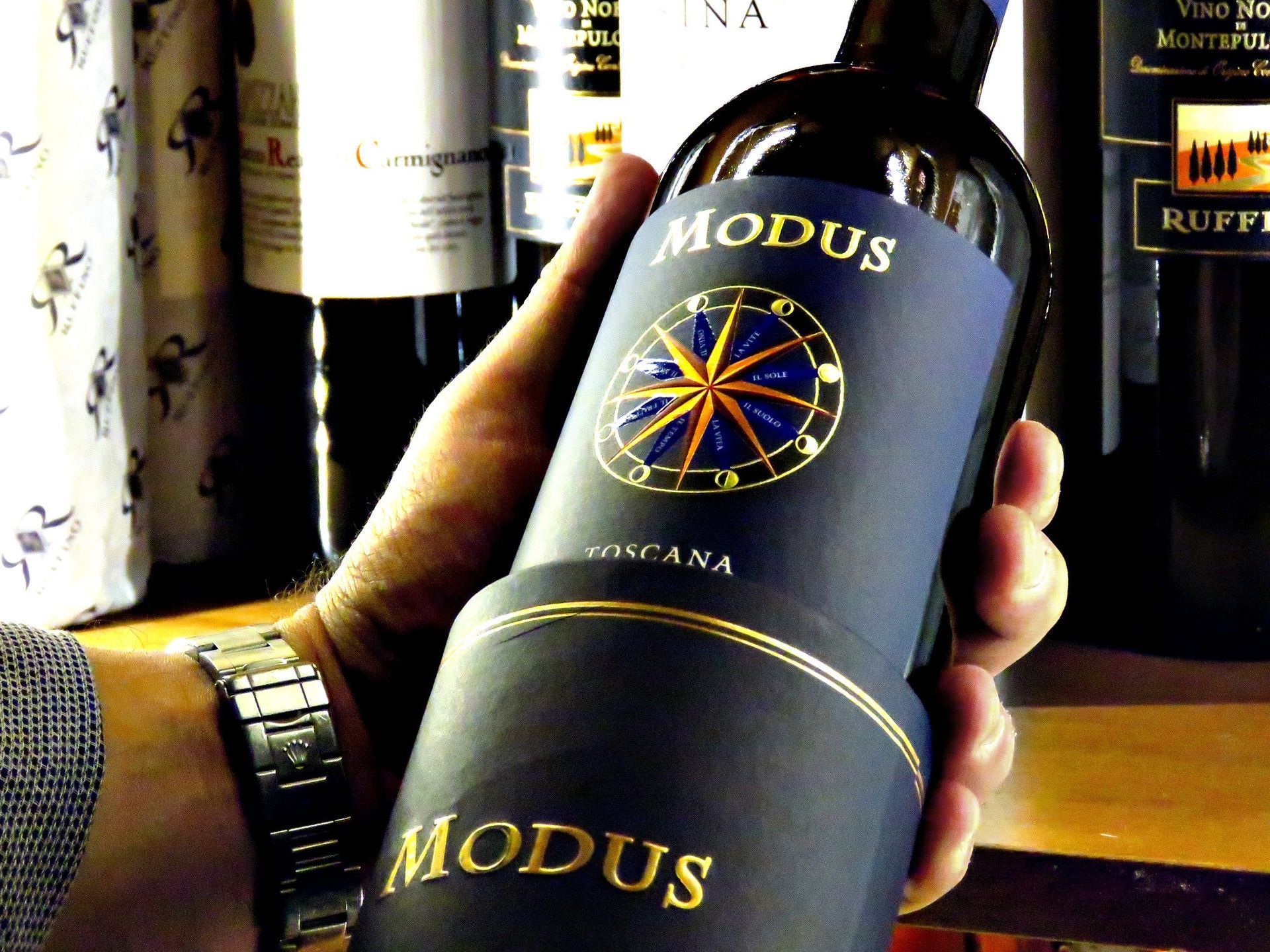 Mano che regge una bottiglia di vino blu scuro con l'etichetta