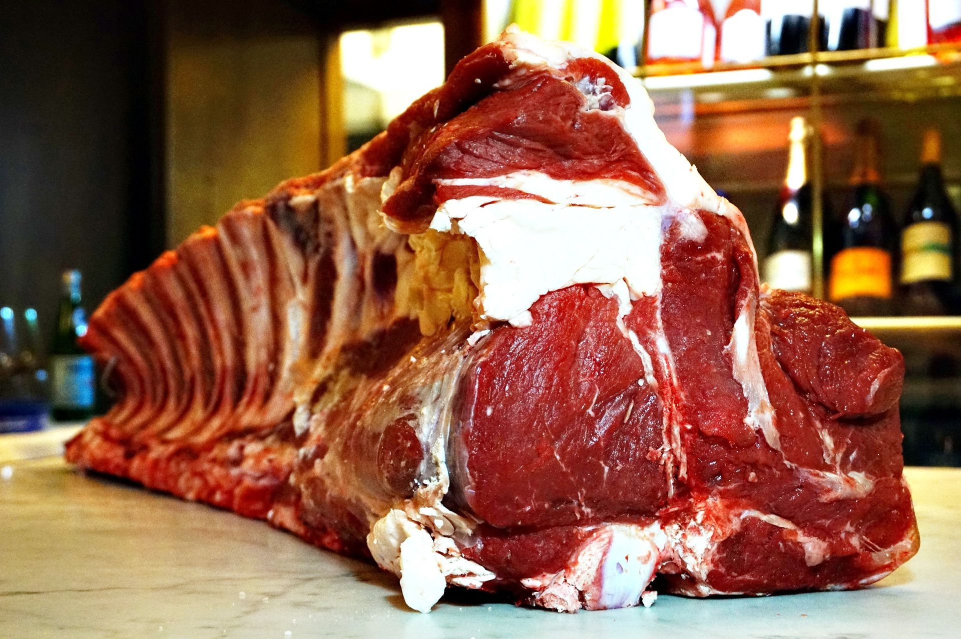 Macellaio che taglia la carne cruda con un grosso coltello su un tagliere bianco.