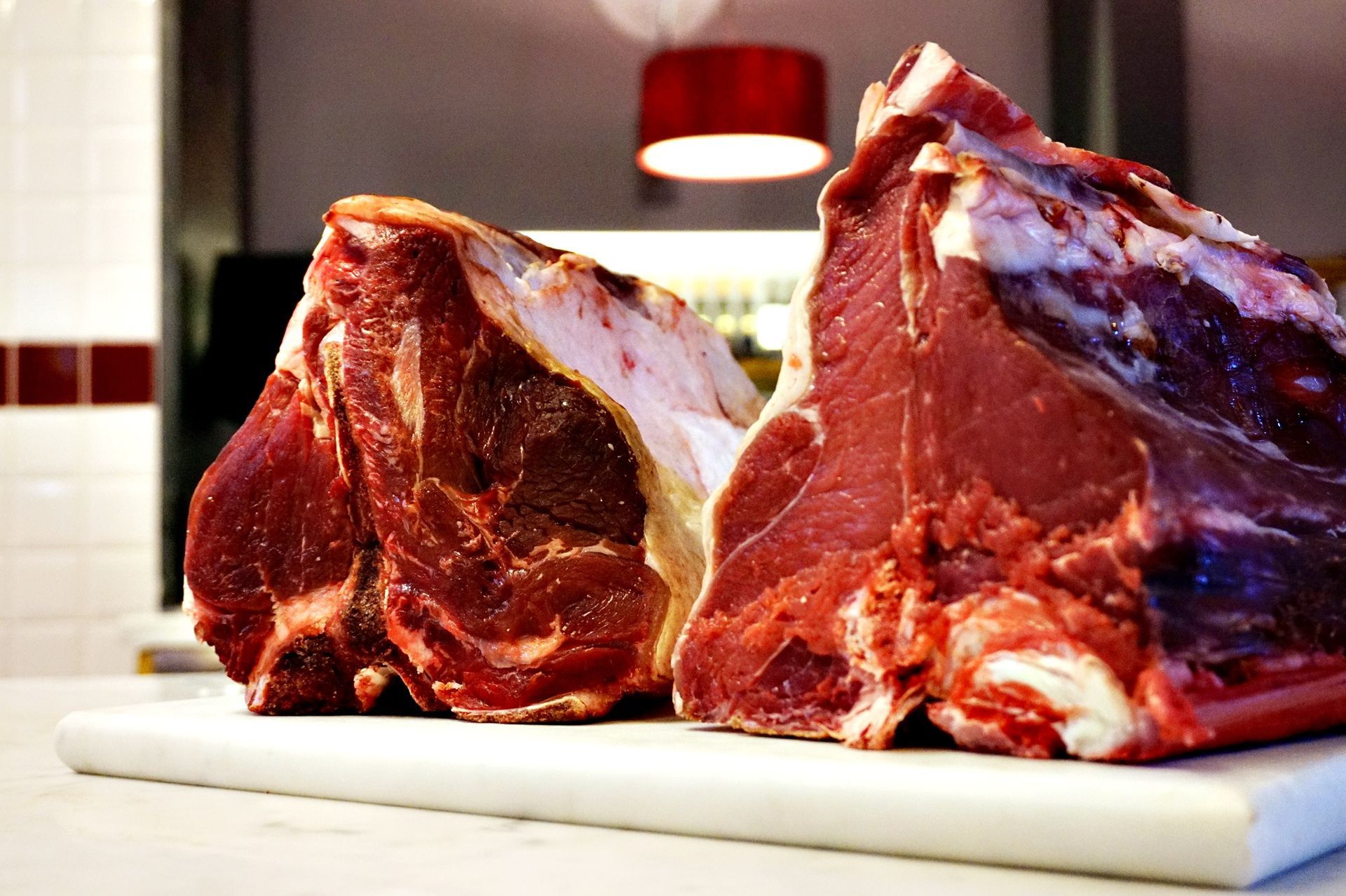 Due grandi bistecche di manzo crude su un tagliere bianco, carne rosso-marrone, grasso bianco, ambiente da cucina.