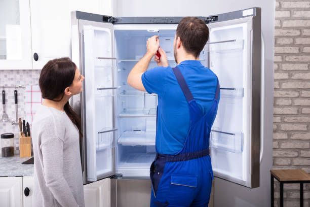 Un técnico arregla un freezer mientras una mujer observa desde una cocina.