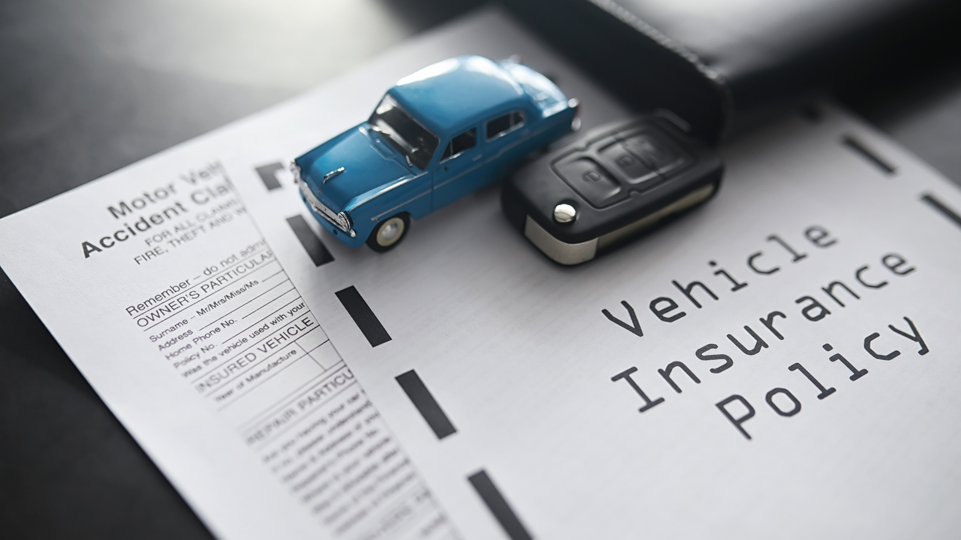 A blue toy car is sitting on top of a vehicle insurance policy.