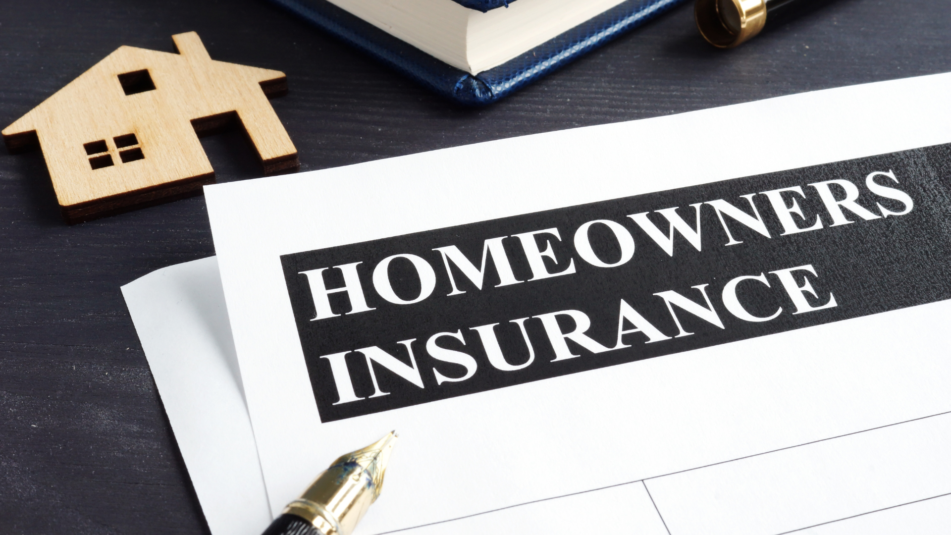 A homeowners insurance form with a pen and a wooden house on a table.