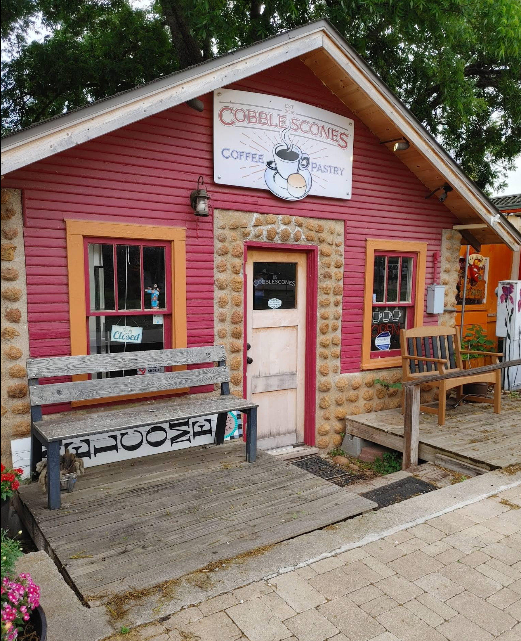 Pink rustic storefront with a white sign, stone doorway, and bench by a cobblestone path