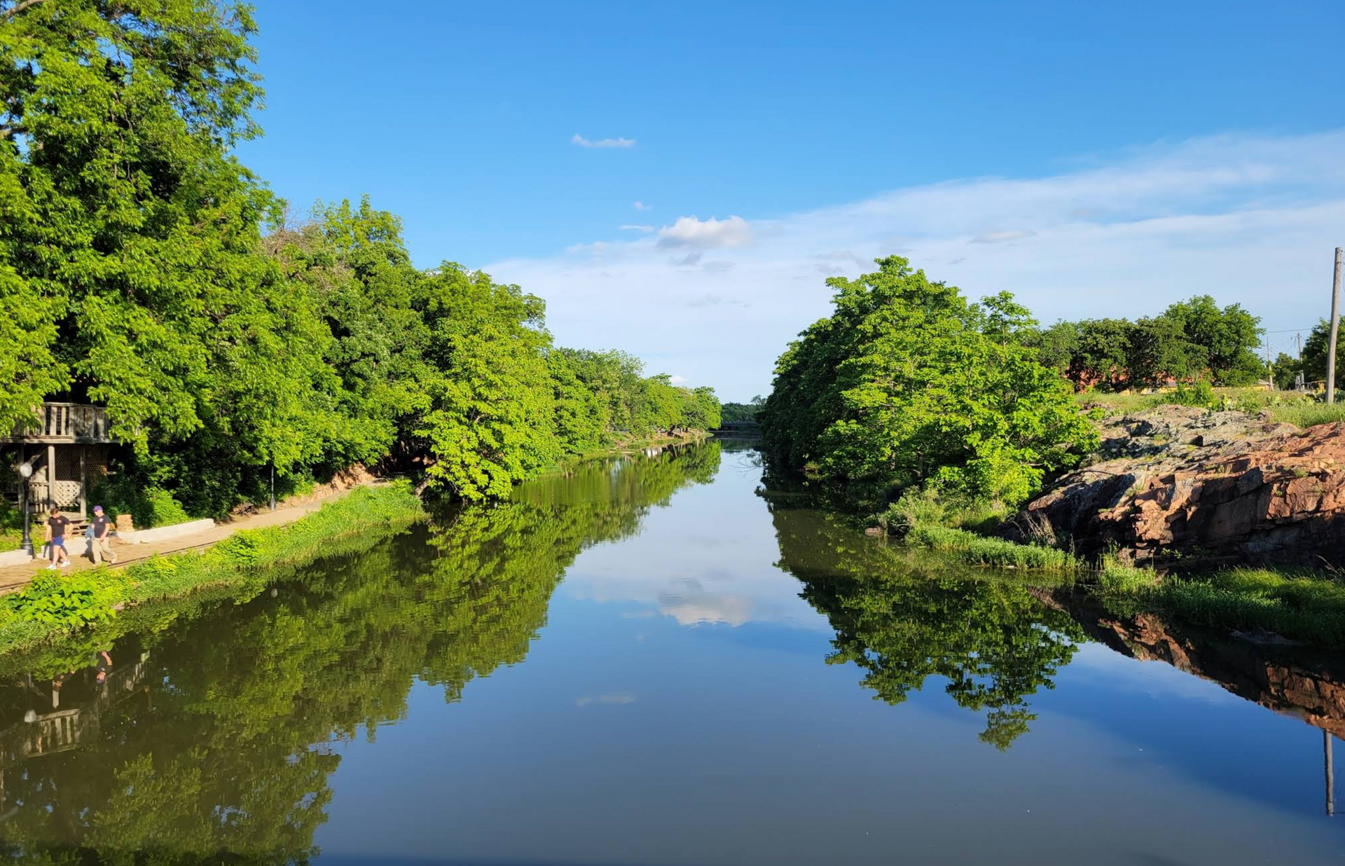 Calm river reflecting green trees and blue sky on a sunny day