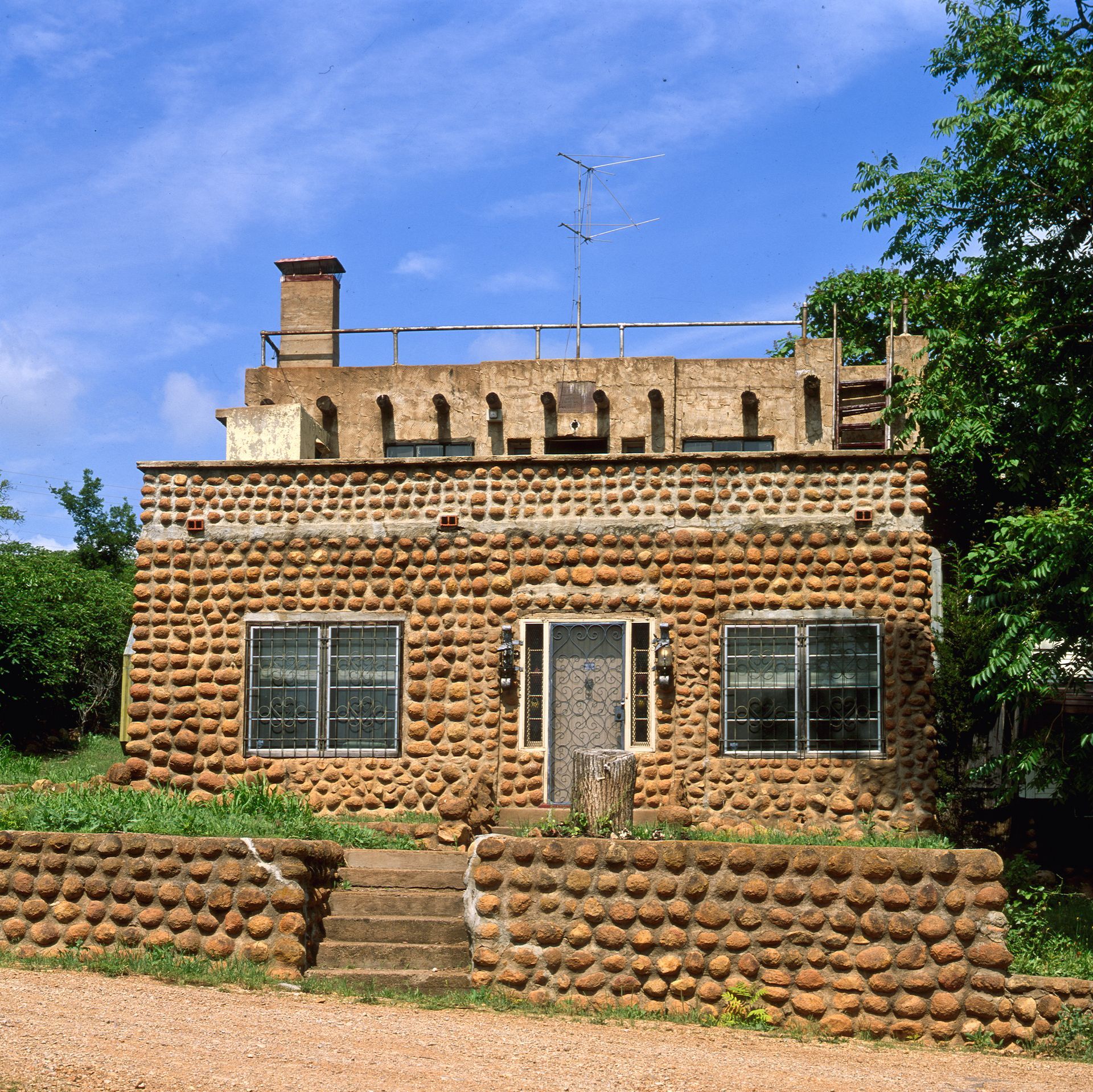 Small brown brick house with a central door and windows, topped by a rooftop antenna under a blue sky