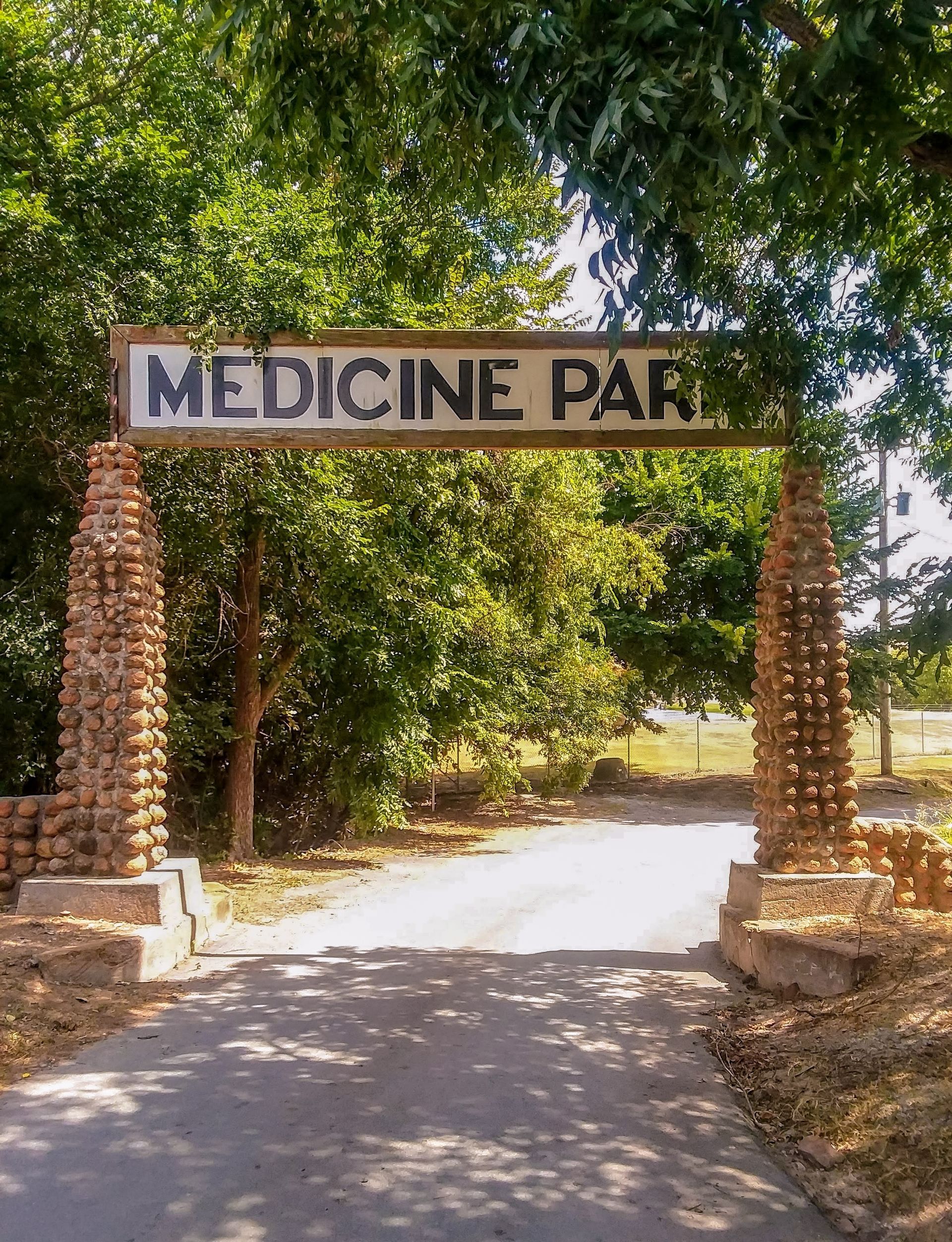 Entrance sign reading “Medicine Park” over a tree-lined path