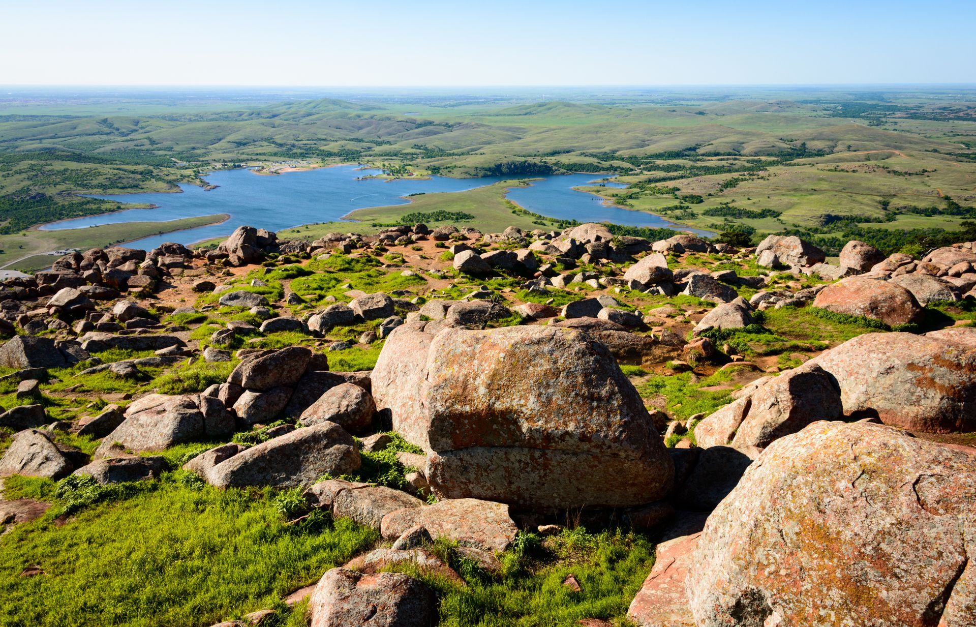 Rocky hillside overlooking a blue lake and green valley under a clear sky