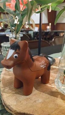 Brown toy horse with white blaze, next to a vase of flowers on a wooden table.